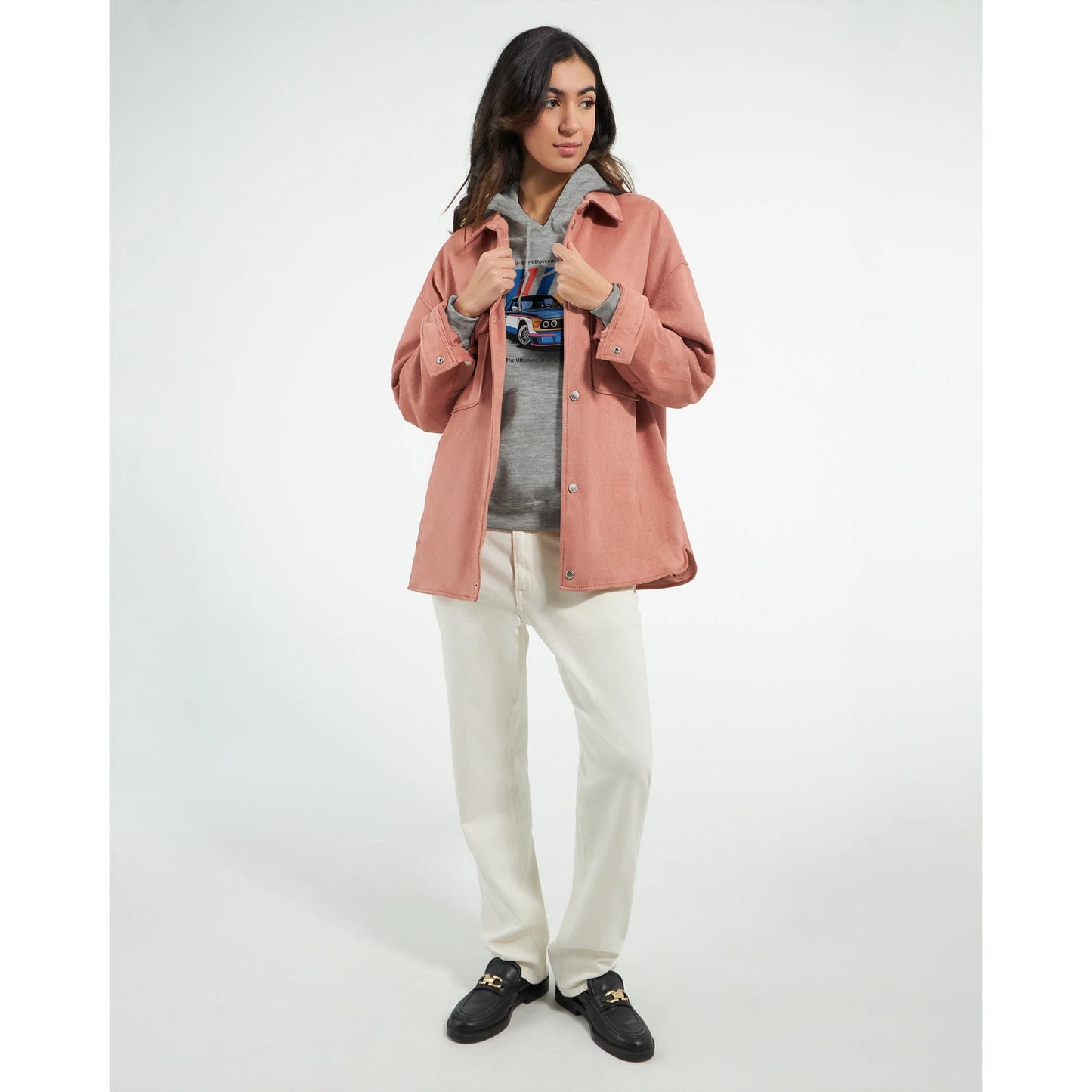 woman wearing born to race unisex grey hoodie with front pouch pocket and drawstring hood under a pink jacket with white pants and black shoes