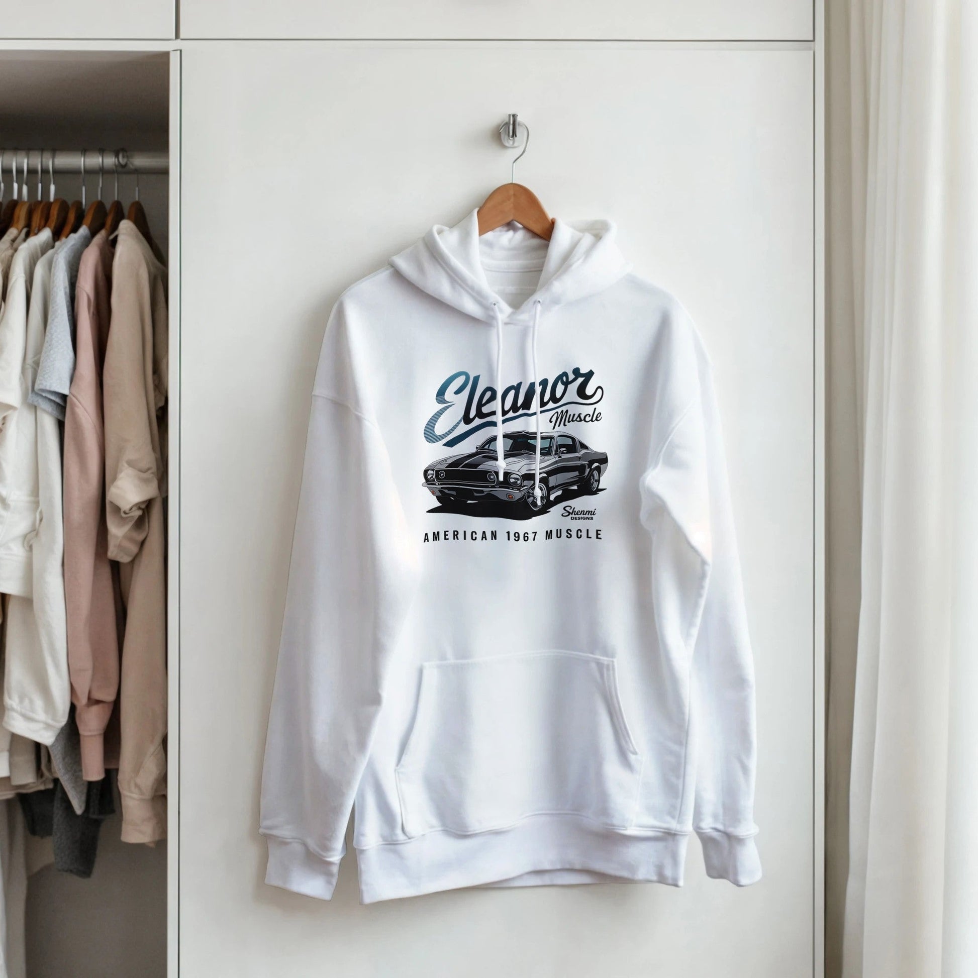 White Eleanor Hoodie with muscle car graphic and text, featuring a front kangaroo pocket and adjustable drawstring hood, hanging in a closet.