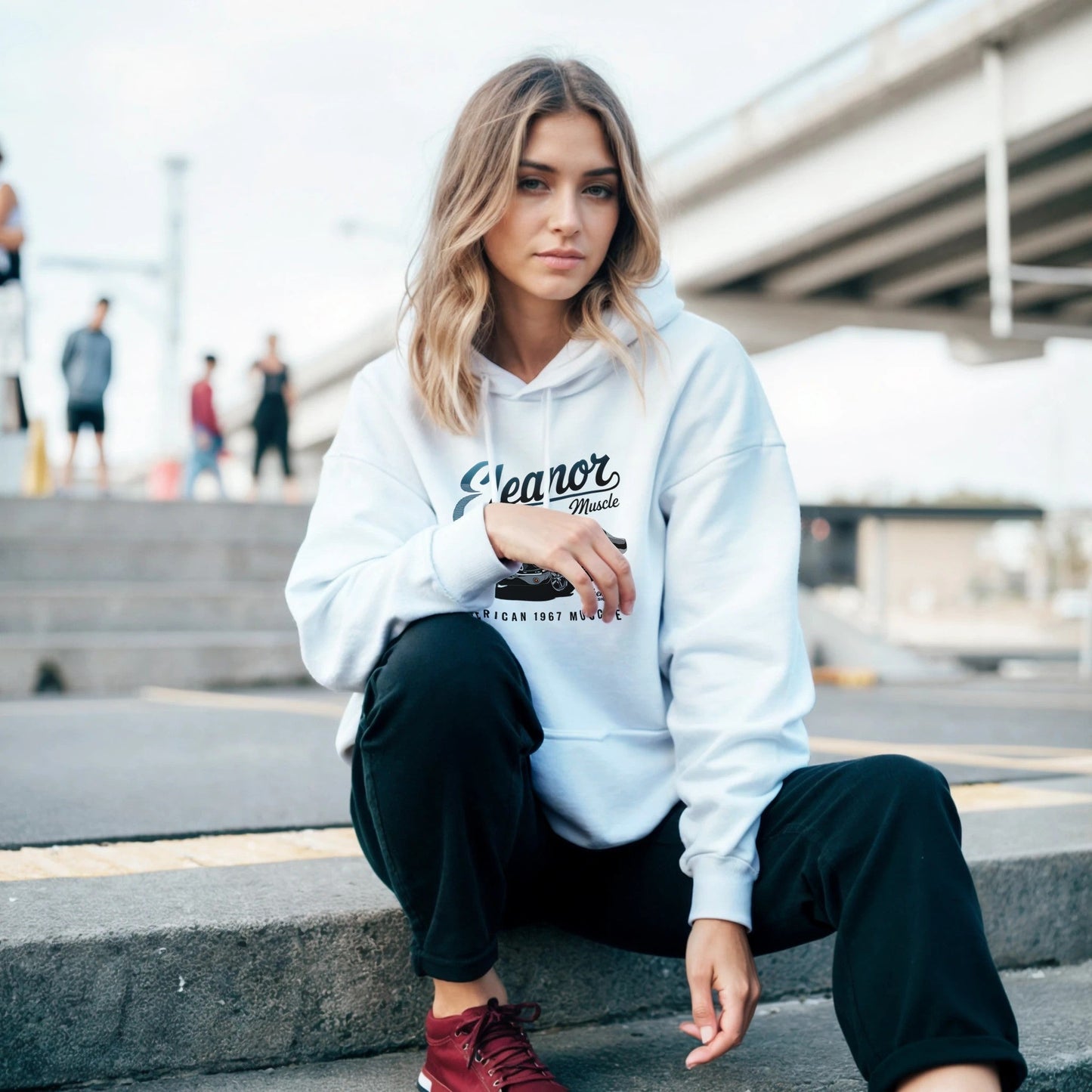 woman wearing white eleanor hoodie with car-themed print sitting outdoors on steps