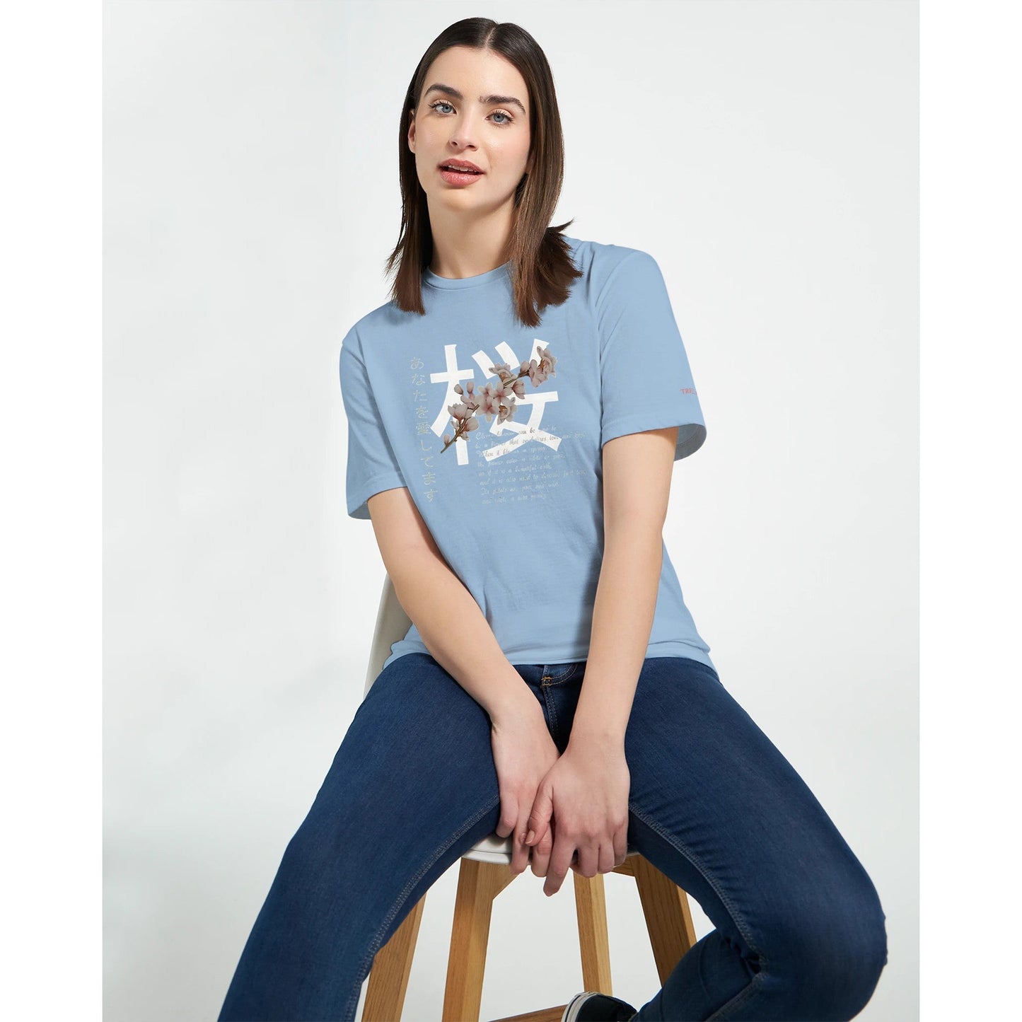 frau trägt hellblaues crewneck t-shirt mit kirschblüten träume design, kombiniert mit jeans, auf weißem hintergrund.