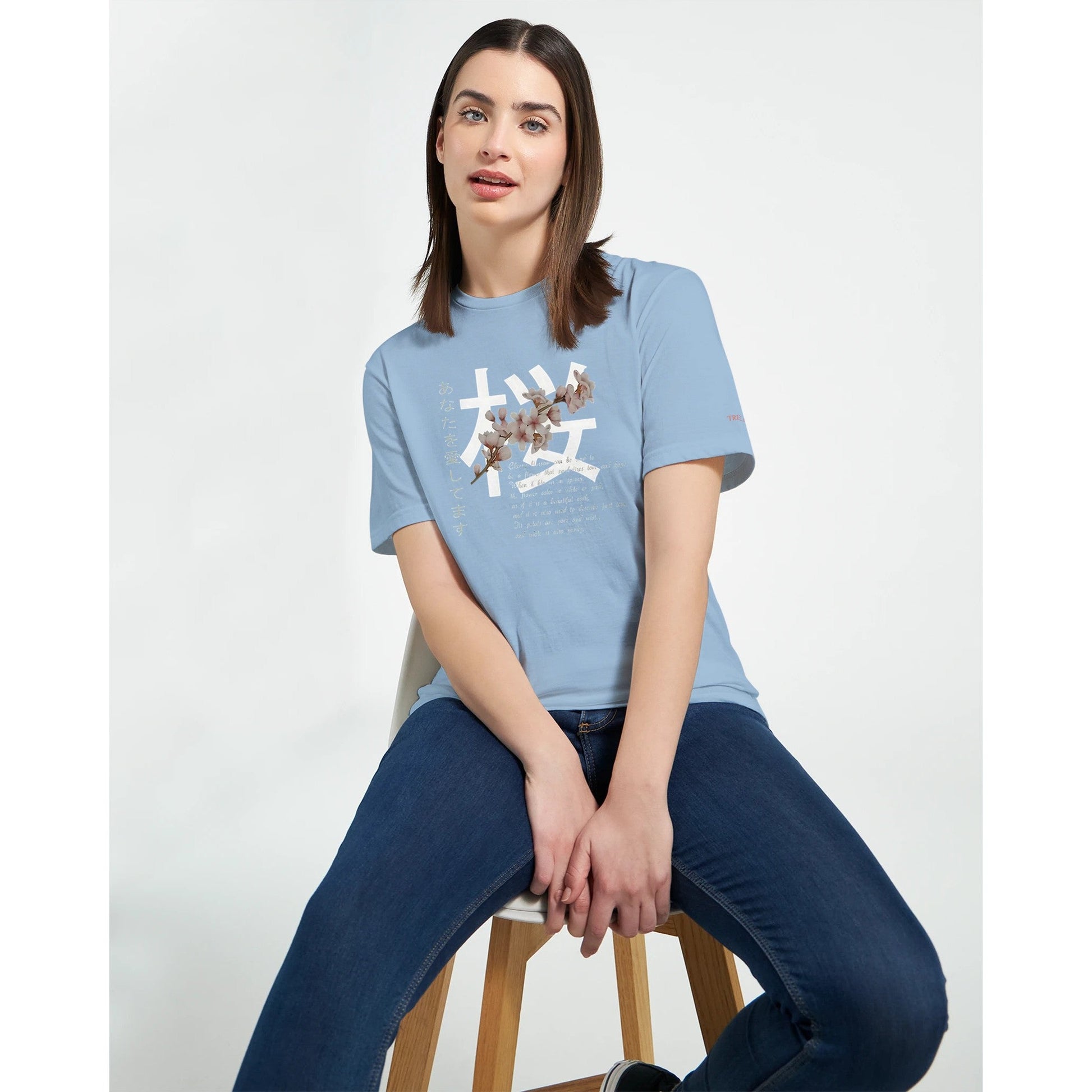 Frau trägt hellblaues Crewneck T-Shirt mit Kirschblüten Träume Design, kombiniert mit Jeans, auf weißem Hintergrund.
