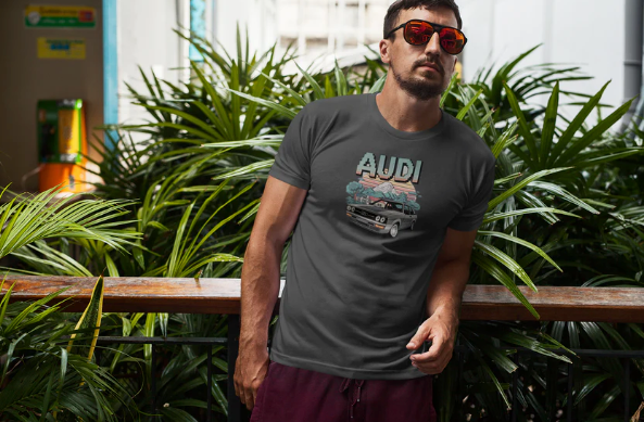 mann trägt oldschool t-shirt minecraft mit audi auto motiv in dunkler farbe, umgeben von grünen pflanzen.