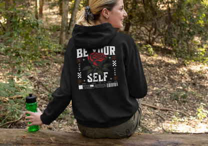 Black unisex hoodie with "Be Yourself" text and red rose design on the back, worn outdoors by a seated person.