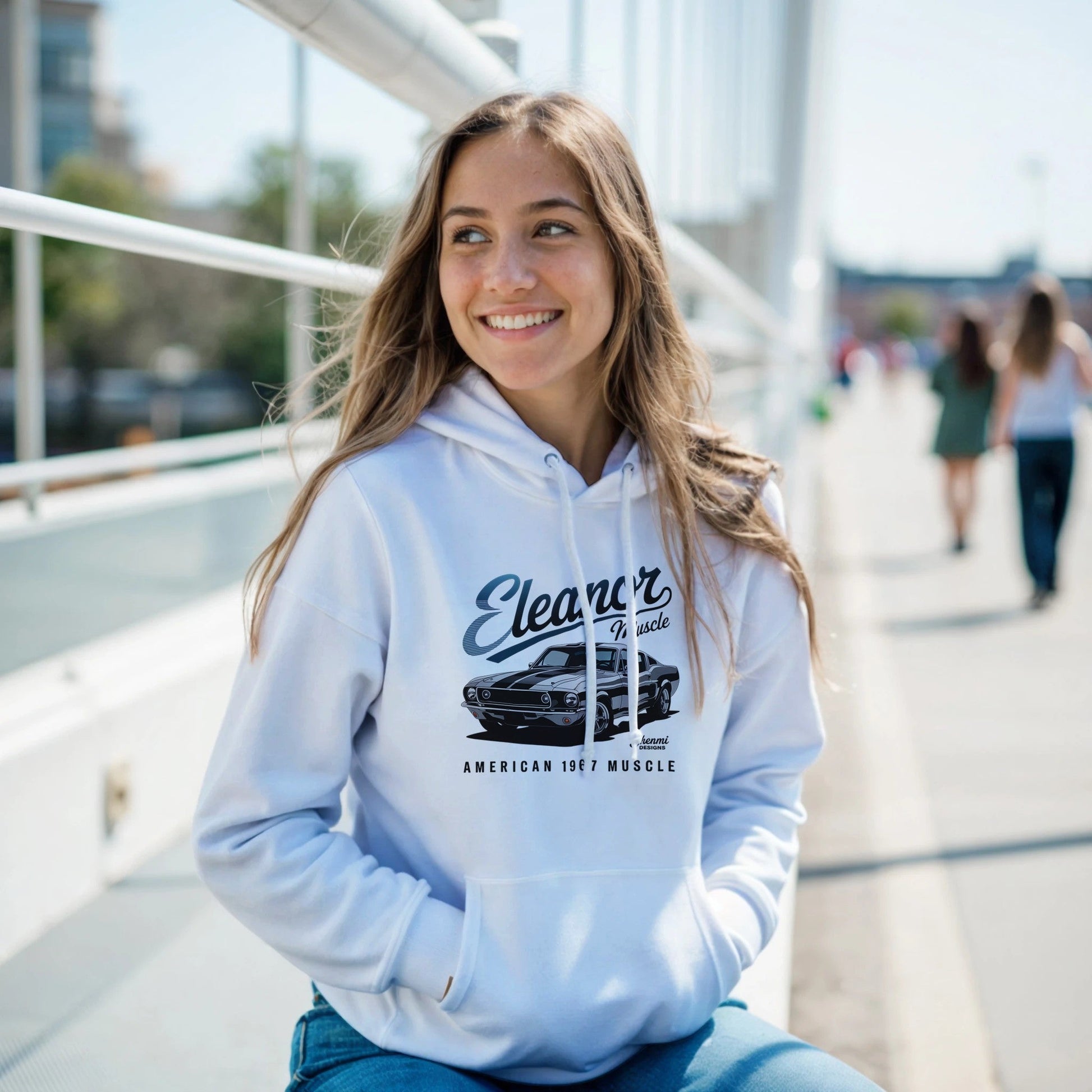 Young woman wearing a white Eleanor Hoodie with muscle car graphic sitting outdoors on a sunny day