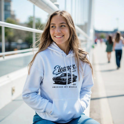 Young woman wearing a white Eleanor Hoodie with muscle car graphic sitting outdoors on a sunny day