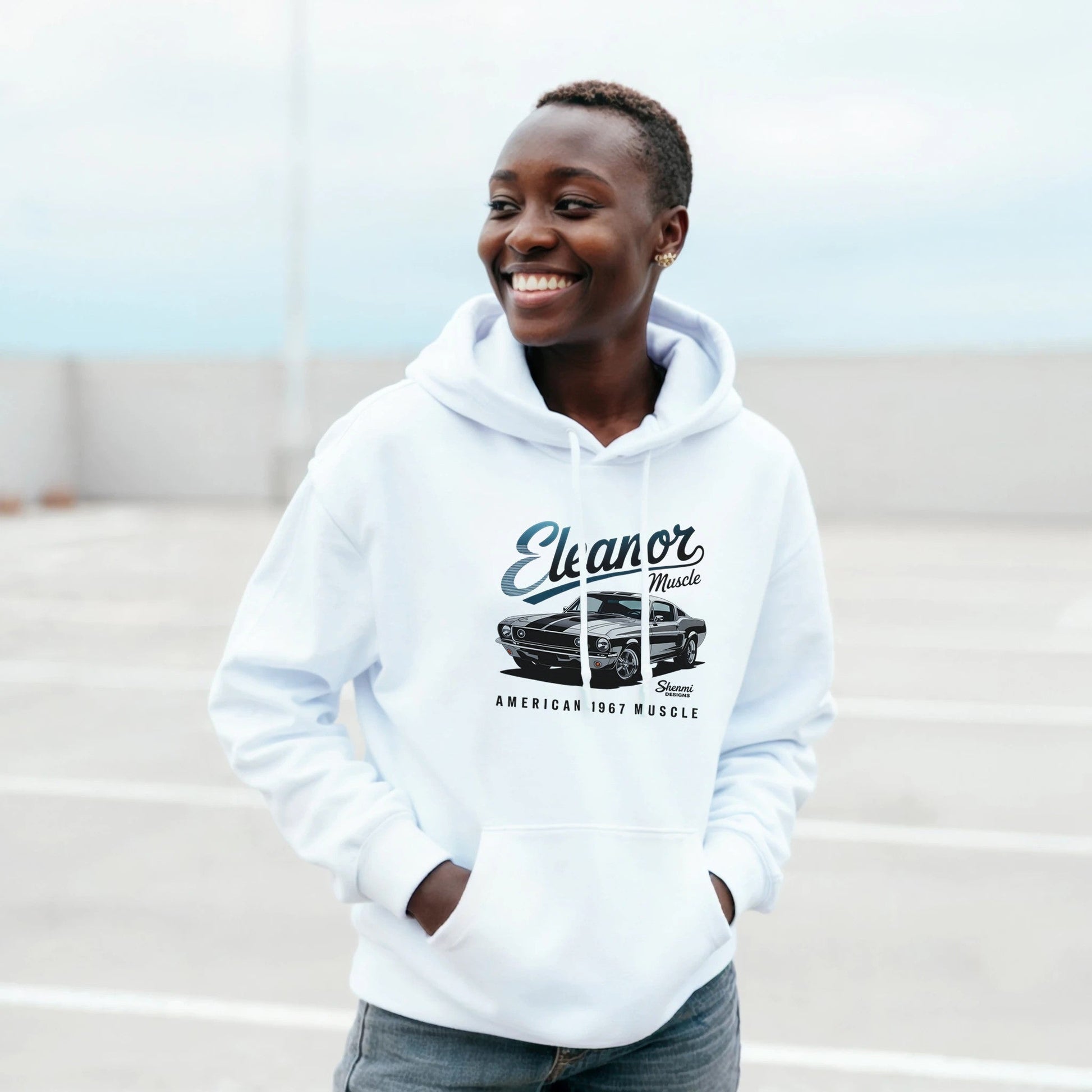 Smiling person wearing a white Eleanor Hoodie with a classic 1967 muscle car graphic on the front, styled for car enthusiasts.